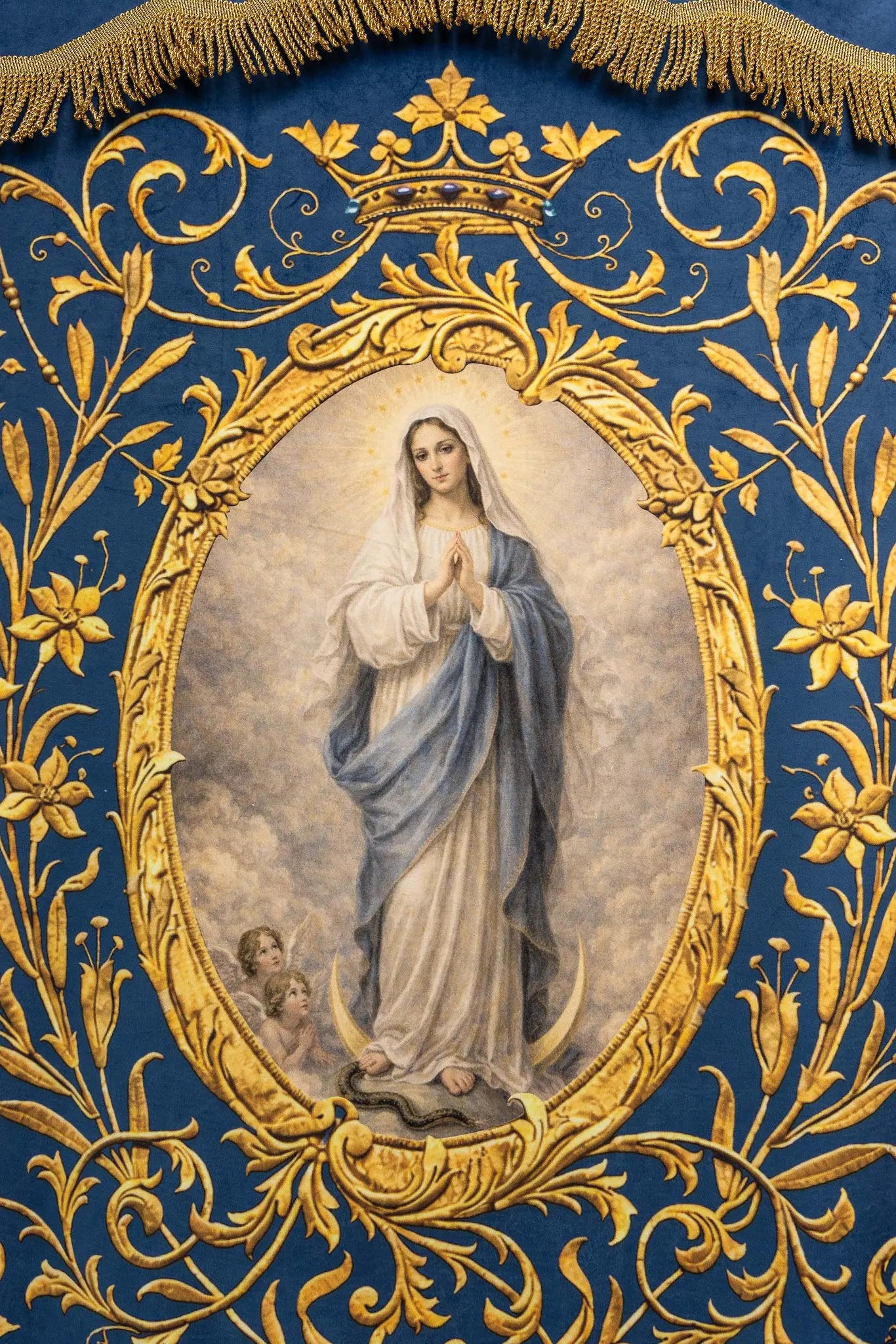 Double-sided blue processional banner with an image of Our Lady of the Immaculate Conception on one side and a Marian monogram on the other, both surrounded by gold floral ornamentation and finished with gold fringes.