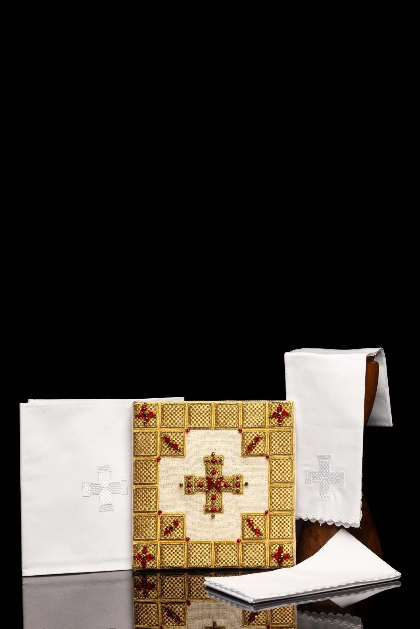 Ecru handmade chalice linen set with a pall featuring a dimensional gold cross, red hematite, and shimmering crystals, a corporal with a central cross, and a purificator and lavabo towel with embroidered crosses, all with scalloped edges.