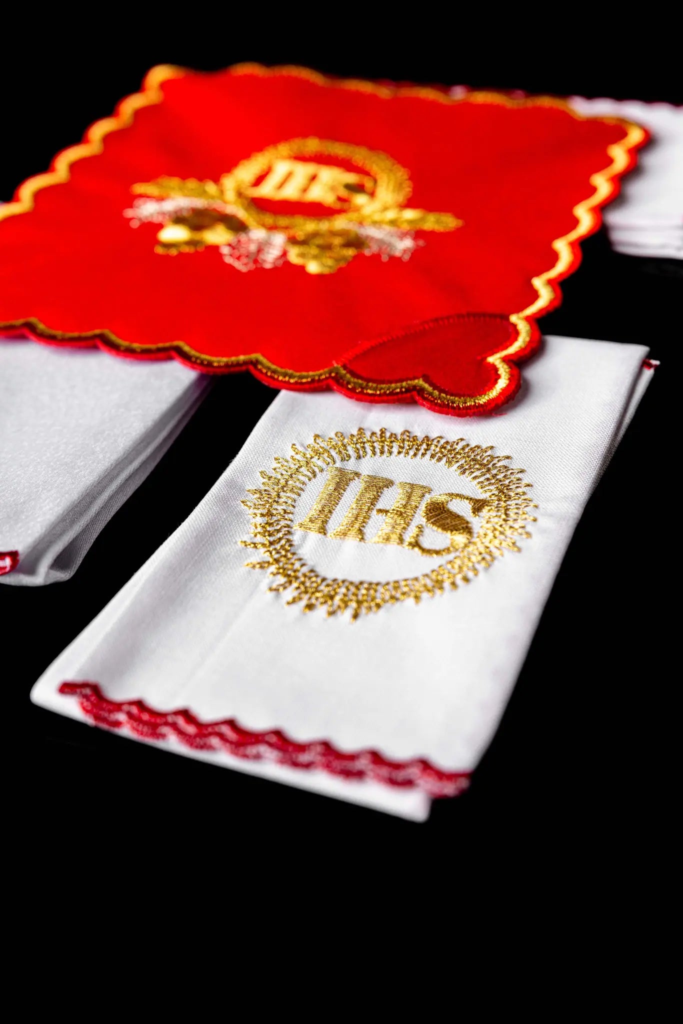 Red chalice linen set with gold IHS embroidery, including a red pall, white corporal, white purificator, and white lavabo towel, all with matching gold IHS symbols and scalloped embroidered edges.