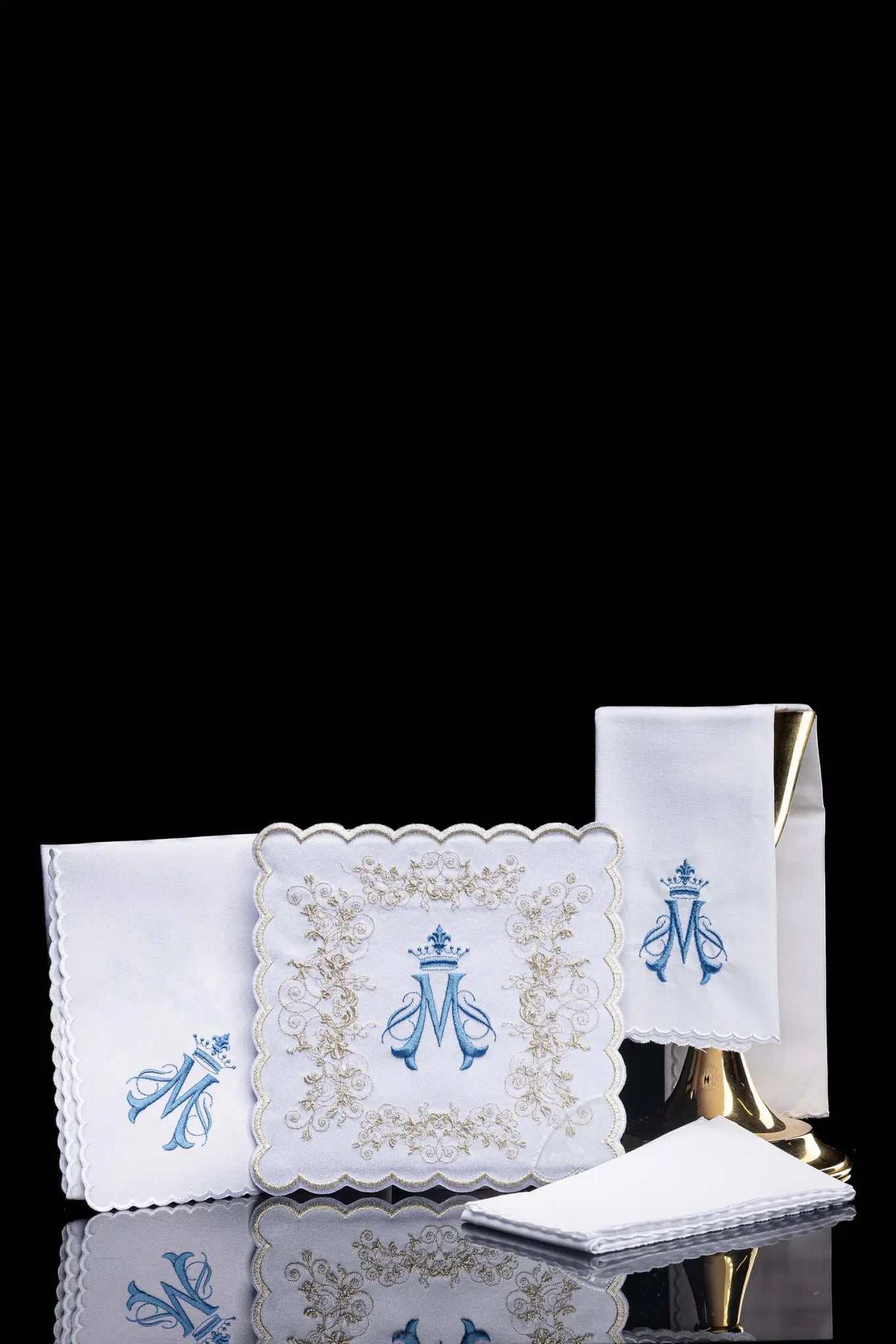 White chalice linen set with Marian monogram embroidery in blue and gold, including pall, corporal, purificator, and lavabo towel.