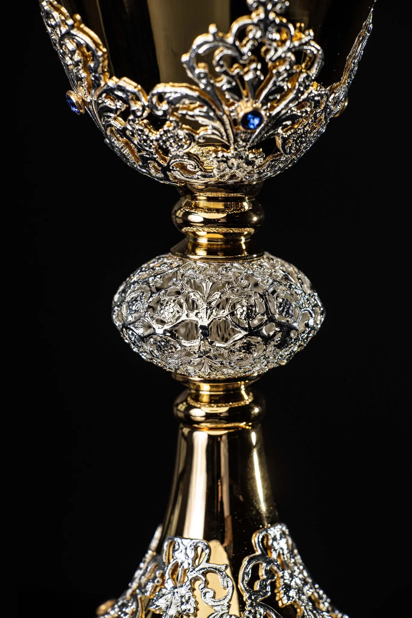 Handmade gold-plated liturgical chalice with silver-plated floral ornamentation and blue sapphire-like stones. The chalice features a decorated cup, nodus, and base.