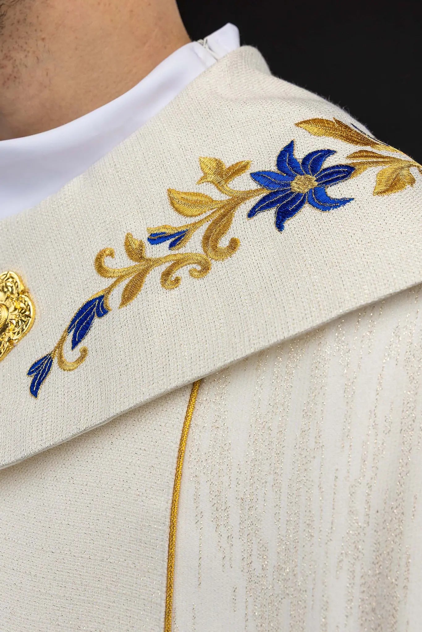 Ecru embroidered cope with Marian symbol, featuring gold and blue floral embroidery, a crowned 'M' monogram, and an ornate gold clasp with chain.