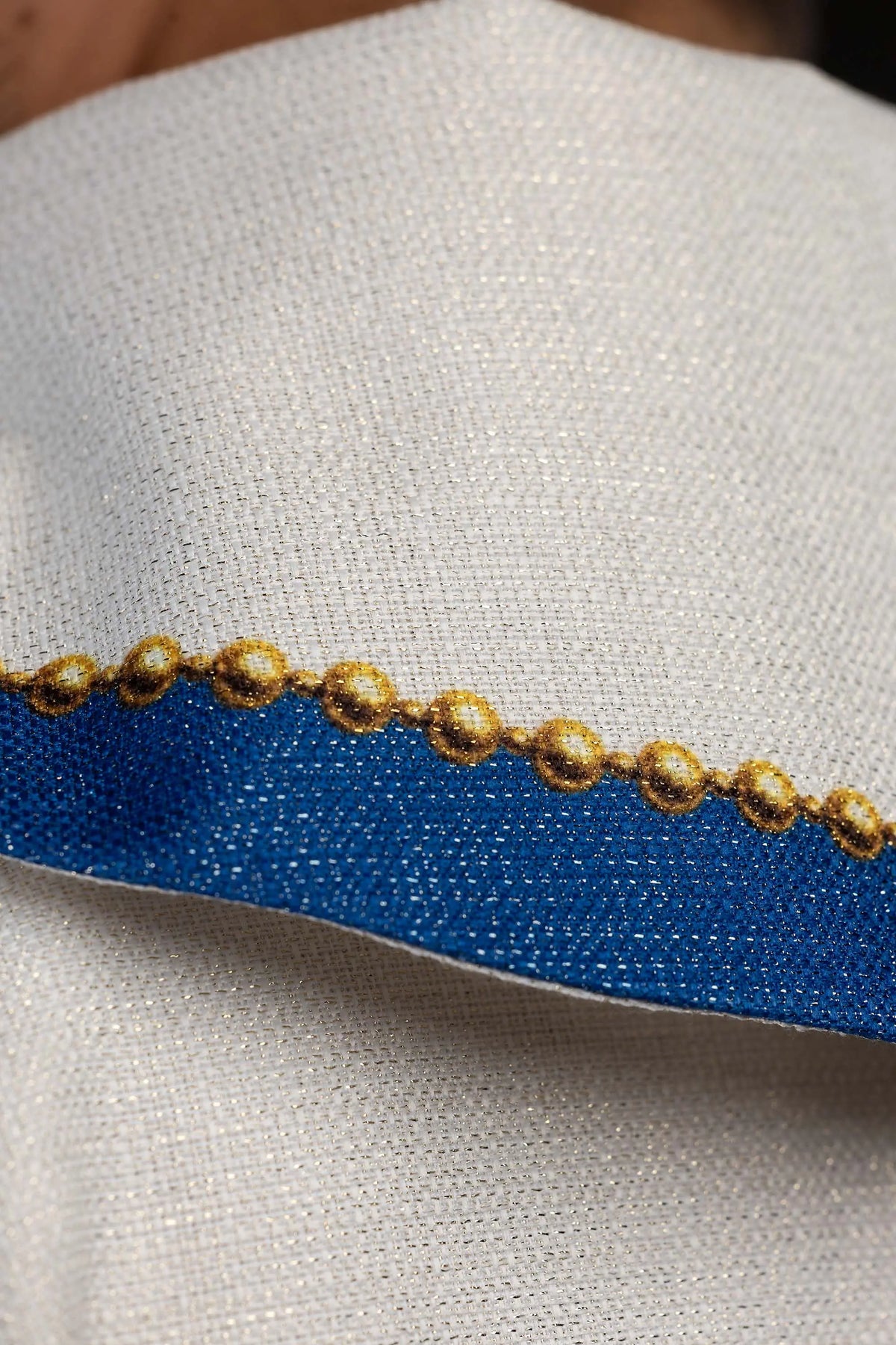 Marfil casulla con ribete azul y cuentas doradas, detalle del tejido