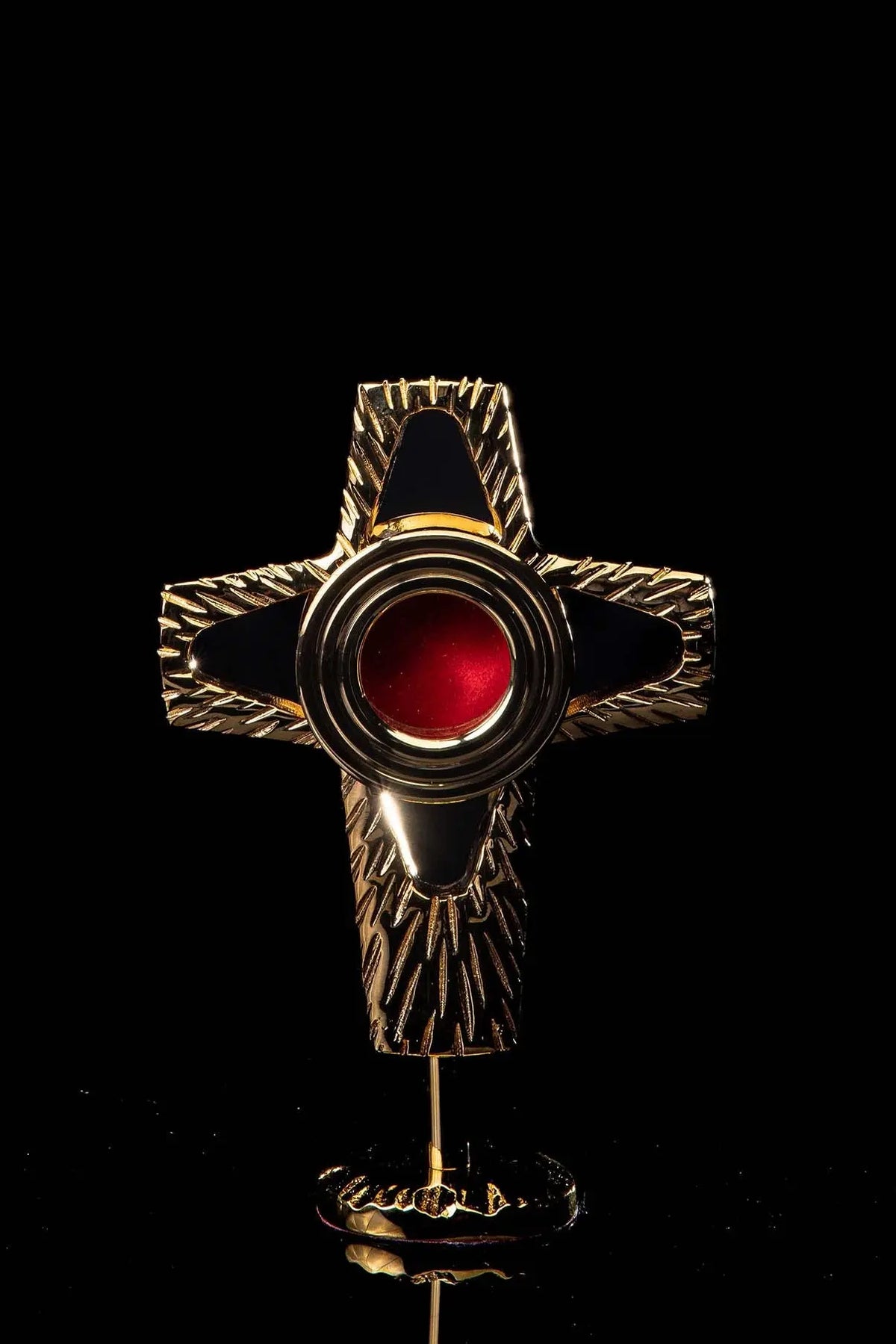 Relicario con forma de cruz de latón dorado con centro rojo, vista frontal sobre soporte