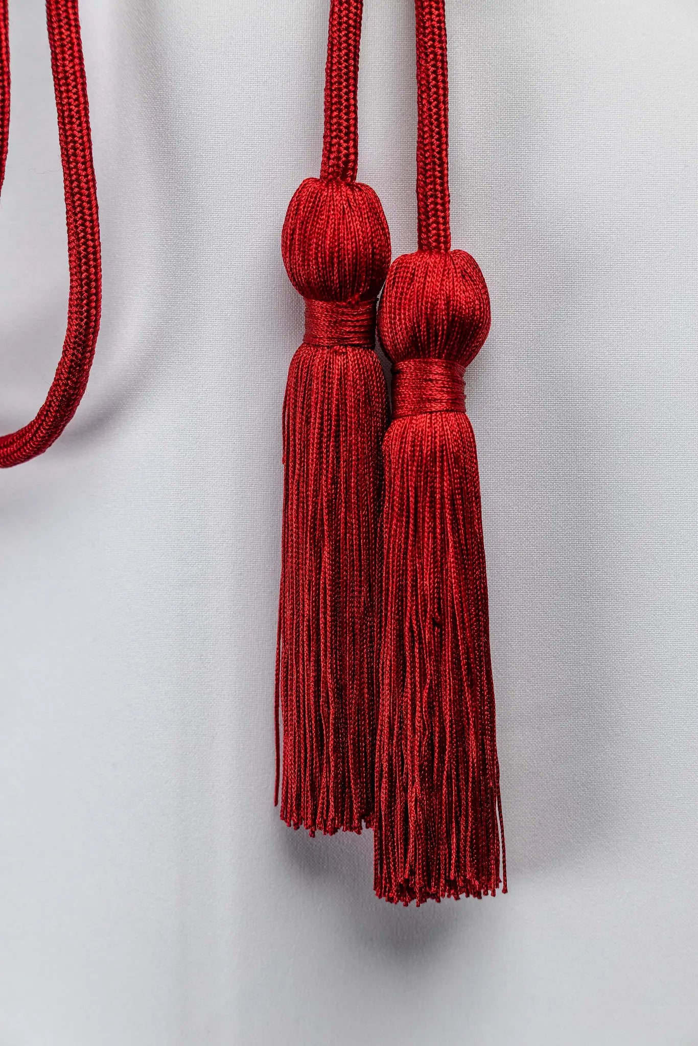 Red liturgical cincture with decorative tassels made from braided cord, tied around an alb.