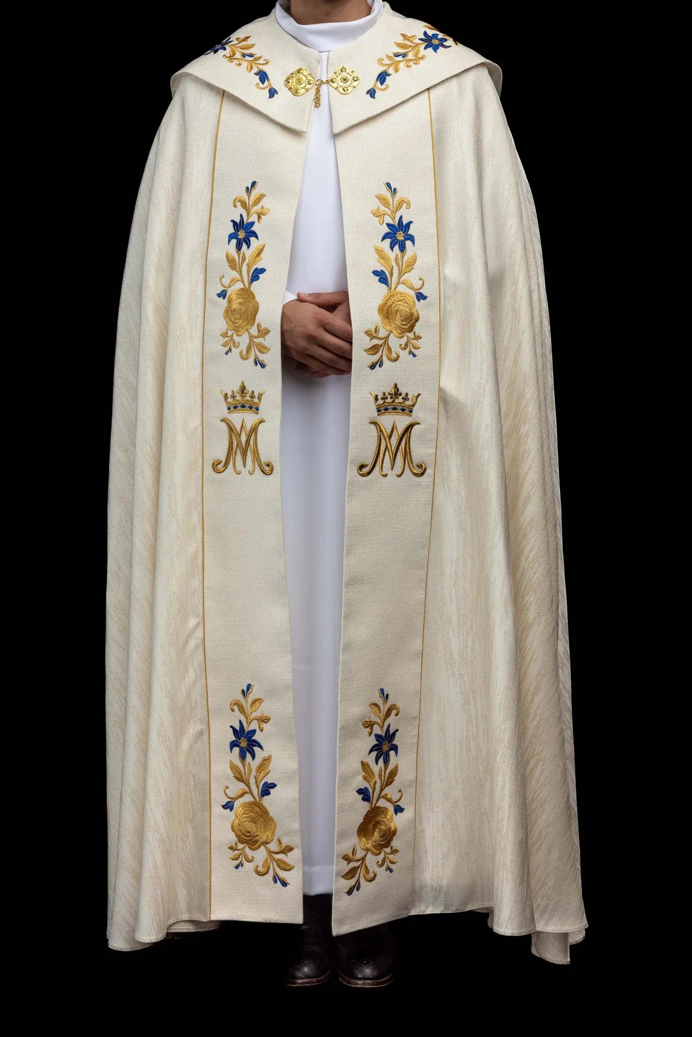 Ecru embroidered cope with Marian symbol, featuring gold and blue floral embroidery, a crowned 'M' monogram, and an ornate gold clasp with chain.