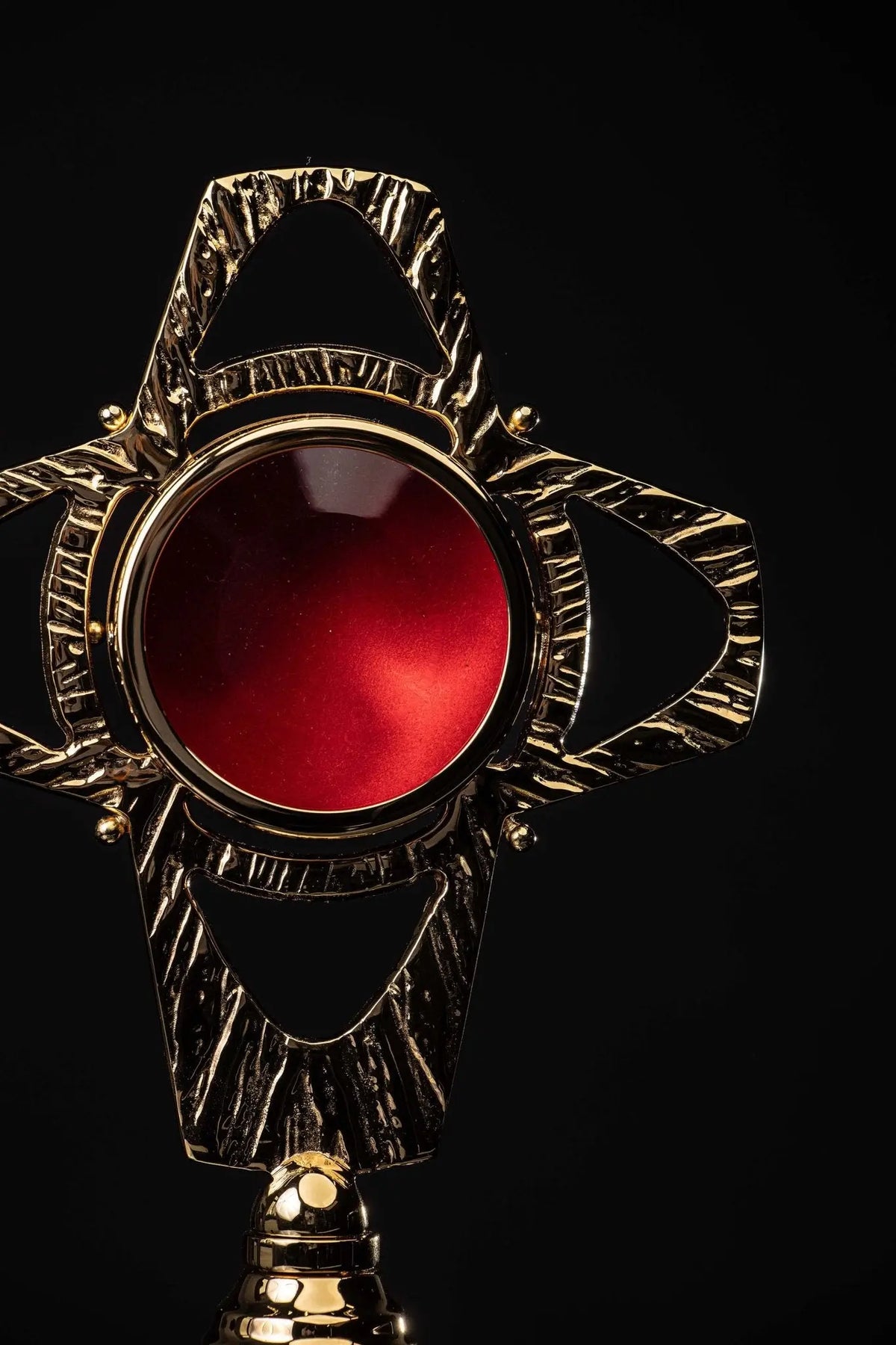 Dorado relicario de latón con forma de cruz, detalle del centro rojo