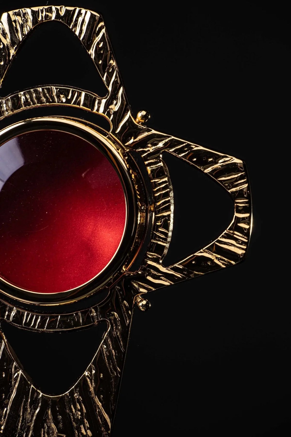 Dorado relicario de latón con forma de cruz, detalle del marco y centro rojo