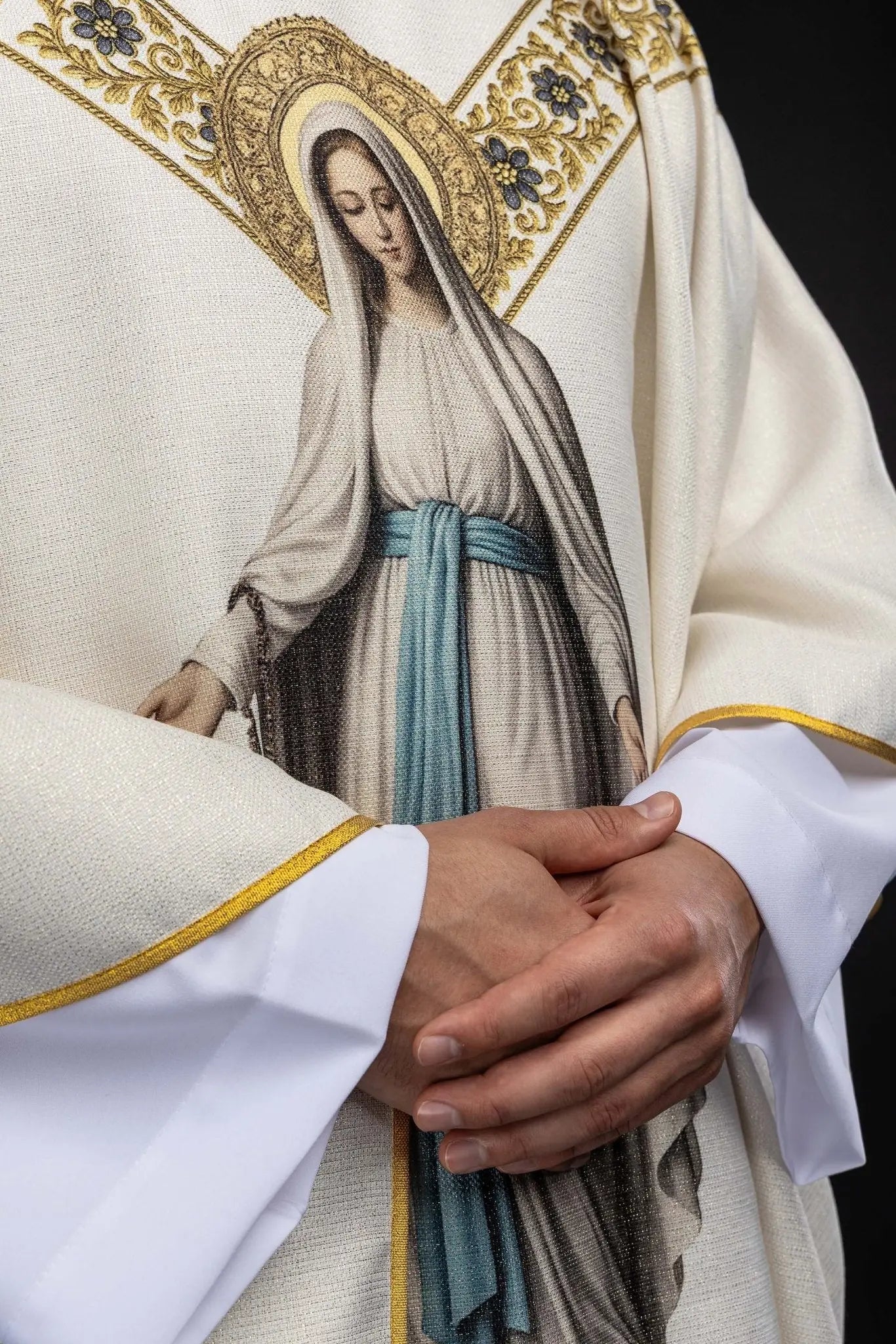 Ecru chasuble with printed image of Our Lady of Lourdes, featuring a blue sash and gold floral motifs, with a matching stole.