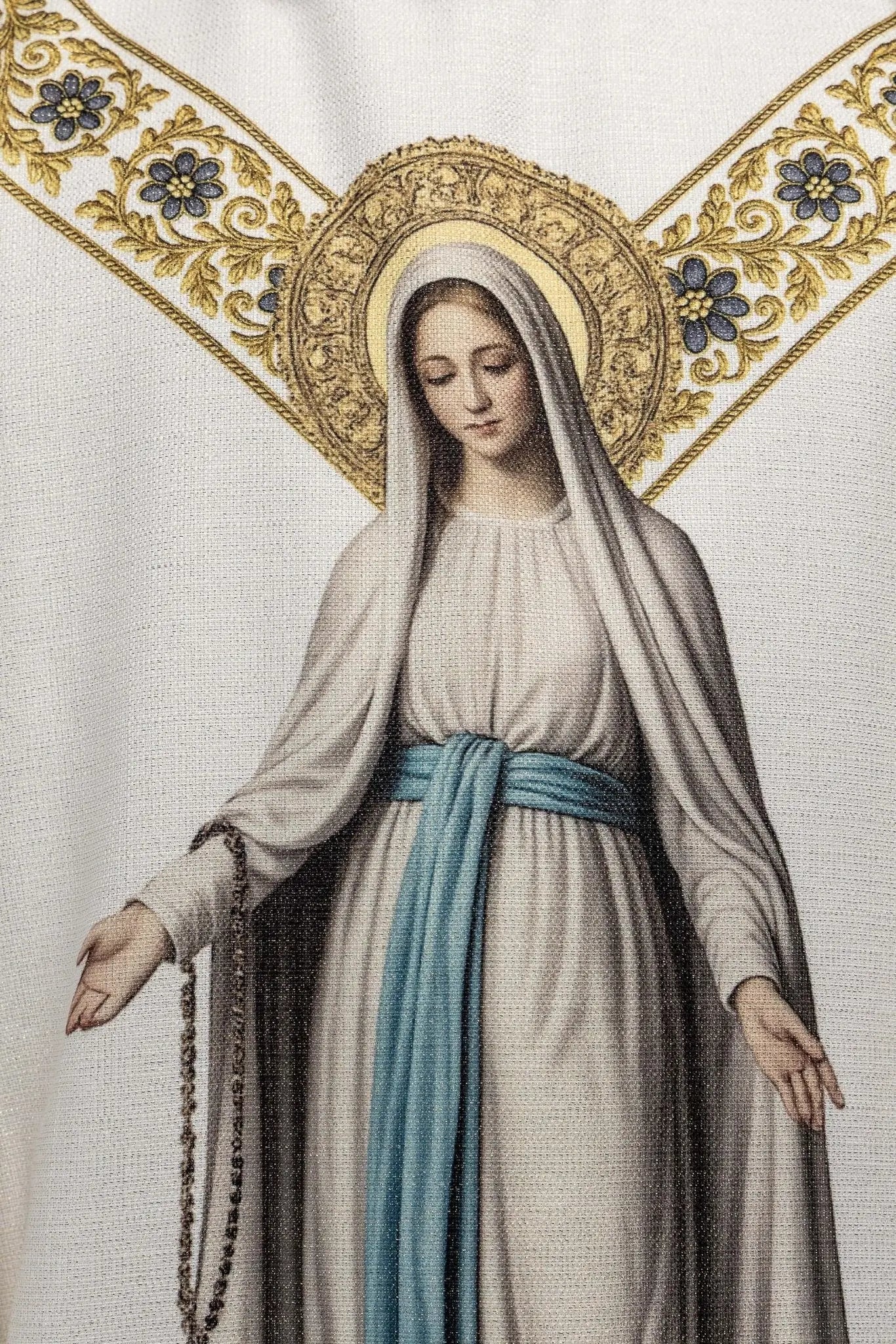 Ecru chasuble with printed image of Our Lady of Lourdes, featuring a blue sash and gold floral motifs, with a matching stole.