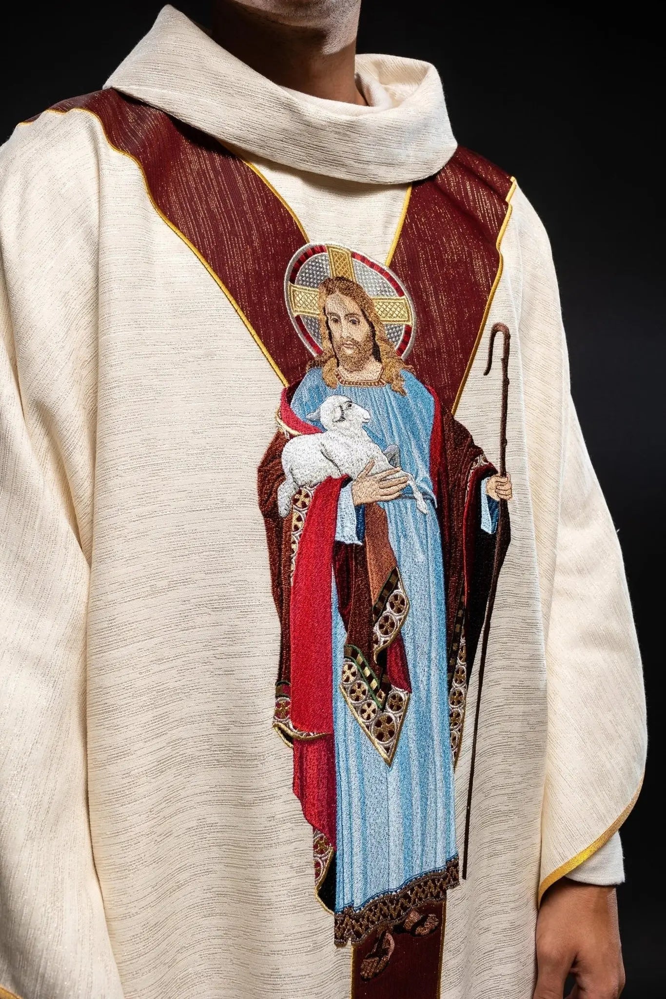 Casulla ecru con la imagen de Jesús el Buen Pastor con una franja decorativa burdeos
